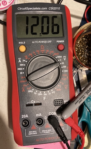 The multimeter shows a solid +12VDC coming out of the power supply.