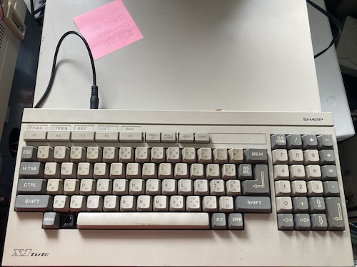 The keyboard is resting on top of the computer, with an ugly black patch cable sticking out of it.