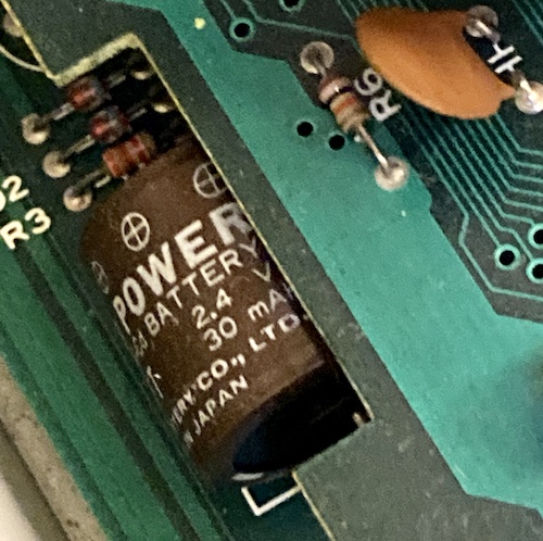 A Yuasa Memo Power NiCad battery (2.4V, 30mAh) is sitting between two boards.