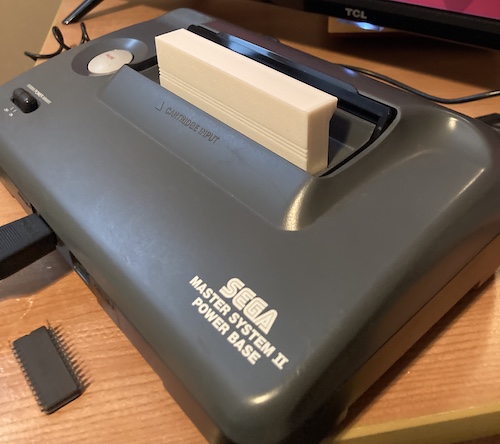 A perfect fit – the cartridge shell is tucked into the Master System 2, just at the right height to read a label, if there were a label. A DIP28 ROM of some description sits upside-down in front of the SMS2, used for some previous experiment and now awaiting ultraviolet erasure and reuse.