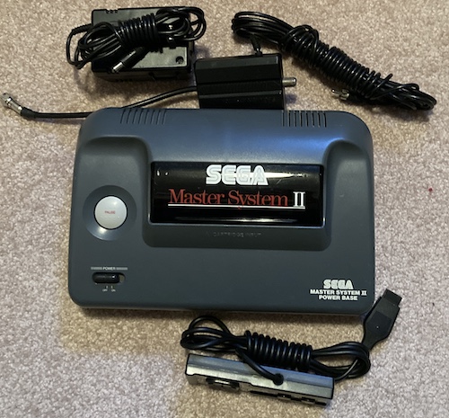 The Master System 2 is freshly out of the seal, and sitting on a carpet. All of the cables are tied up.