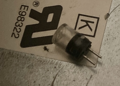 The blown U2 fuse, removed from its socket, sitting against the top of the power supply.