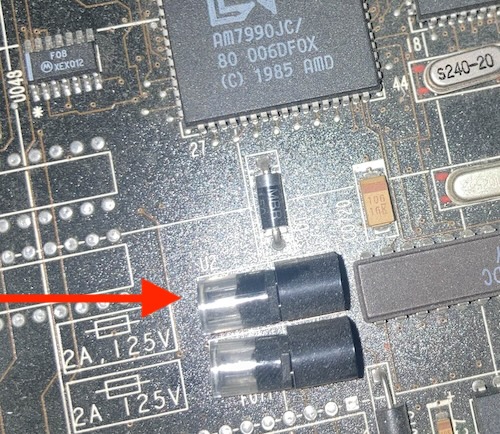 Two socketed round plastic fuses are positioned next to the AMD AM7990 Ethernet controller of the computer.