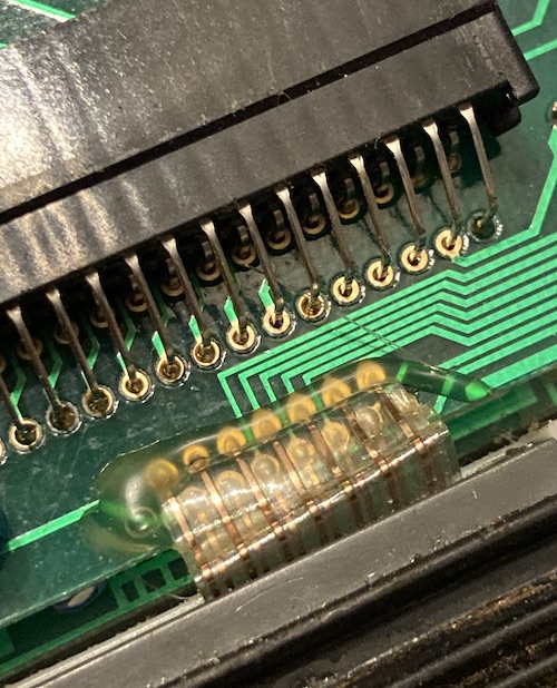The cartridge slot, top side. None of the pins have a good through-hole fillet of solder. Some are clearly loose. A grotesque ribbon cable has permanent folds in it and is hot-glued down to the board.