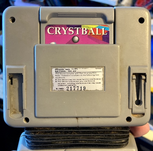 The back of the screen half of the unit, showing grit and grime in every crevice and the missing desk peg. A Crystball cartridge is inserted.