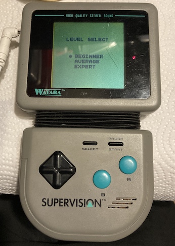 The Supervision, showing the difficulty select screen for Crystball. You can see a little bit of the rusty speaker poking out through the grille.