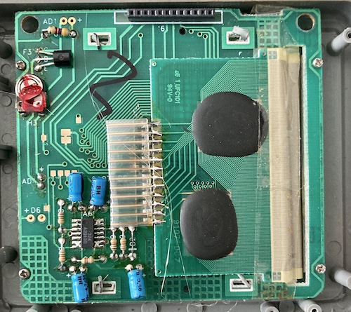 The back side of the Supervision's LCD board; you can see strands of hot glue, some unpopulated pads, and all the interesting stuff is under more glob tops. Some crude folded-over metal tabs pin the board to the LCD assembly.