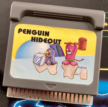 A cartridge of Penguin Hideout. A penguin is pushing a giant ice cube while pursued by a devil holding a giant rice-pounding mallet.