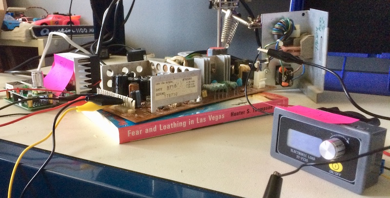 The Tandy 1000SX PSU testing setup, on my desk. There is a maze of wires around and it looks like a mess. The power supply under test is isolated from the ground by a copy of Fear and Loathing in Las Vegas