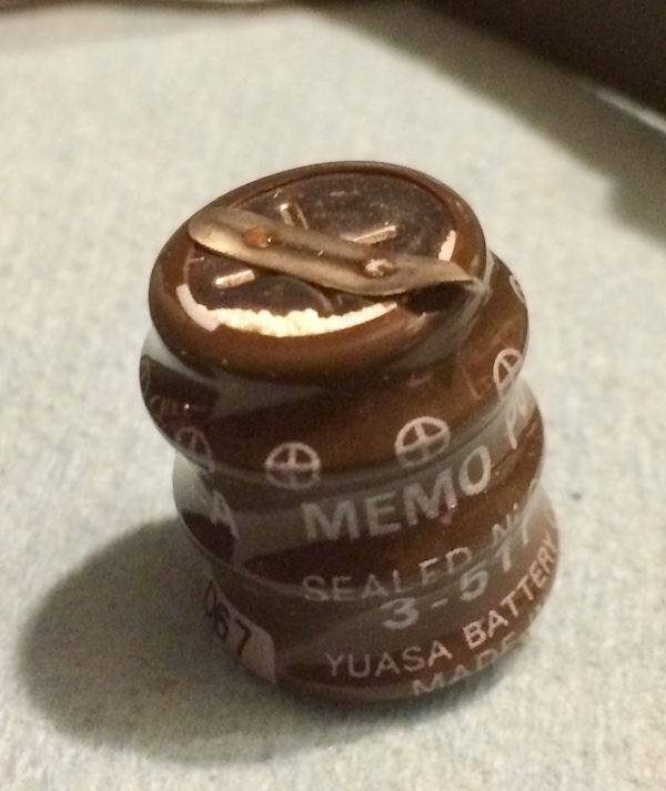 The Yuasa Memo Power battery, removed and on my desk. The positive terminal is shown, leaking some white battery electrolyte around the crimp.