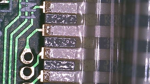 A microscope close-up of the ribbon cable where it is adhered to a pad.