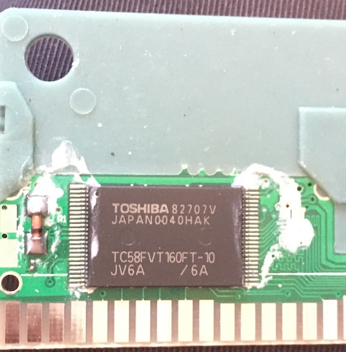 The flash chip on the board, surrounded by more white goopy flux. It reads TOSHIBA TC58FVT160FT-10