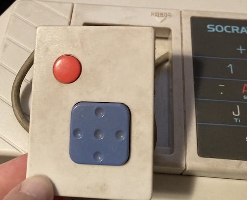 A gamepad comes loose from the keyboard. The cord is dark grey with dirt, and so is the face of the gamepad itself.