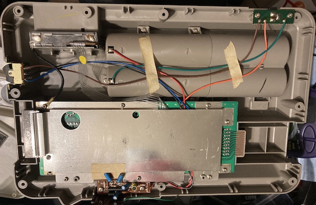 The top case is removed, showing the massive amount of the case taken up by D-cell battery holders. There's wires running everywhere, some held on by masking tape, others with hot glue. A fragile-looking ribbon cable runs to the RF modulator in the back.