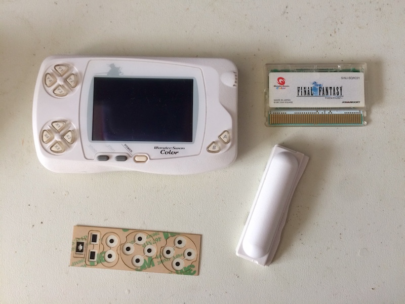 The WonderSwan, with battery and cartridge removed, and the replacement membrane sheet in front