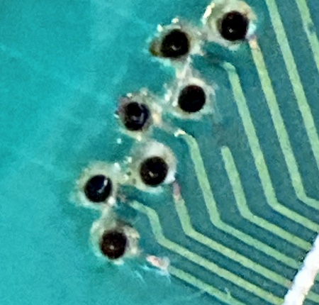 A trace running from a via towards the IOSC is partially missing. There is some shiny exposed copper where the solder mask has been mechanically removed.
