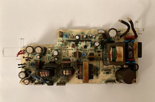 The original power supply is laid up on the paper printout of the new supply outline. Screw holes and the outline match exactly.