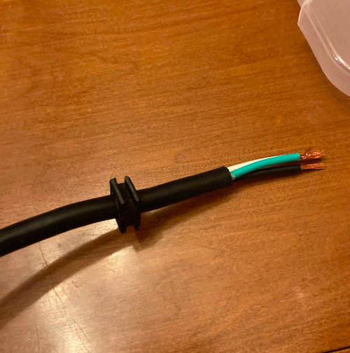 The grommet is pulled onto the black insulation of the power cord. Black, white, and green wires can be seen inside the power cord.