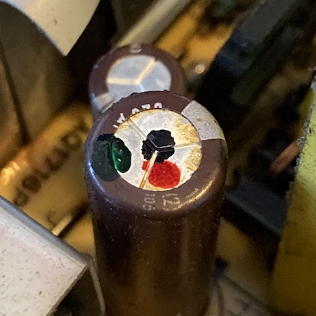 The top of an electrolytic capacitor has some brown-yellow stains near the edges.