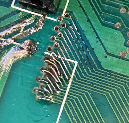Nine traces are patched with solder-covered wire. Other traces, not yet repaired, are scraped free so you can see the bare copper.